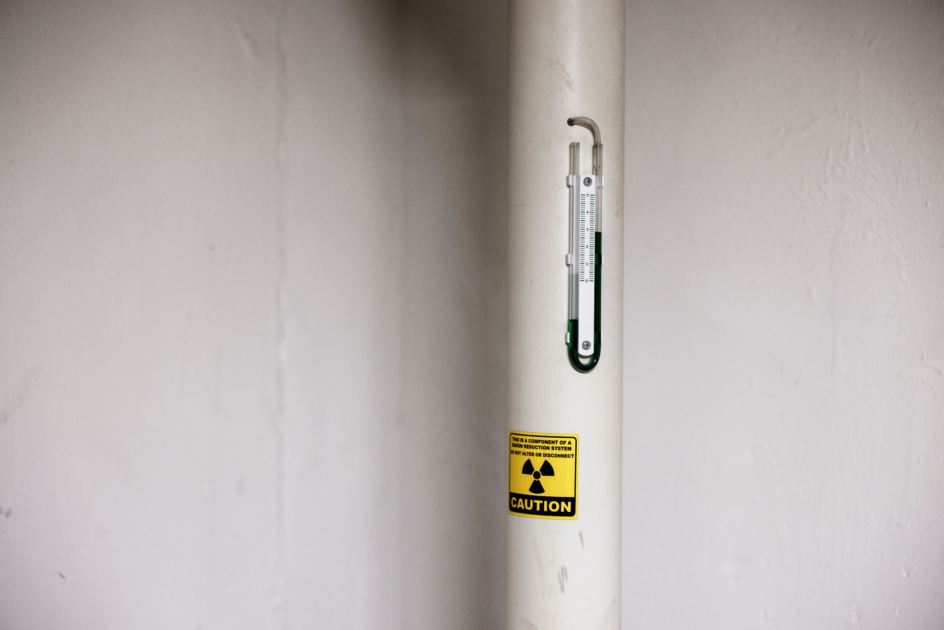 Radon mitigation system pipe with manometer and warning label on basement wall